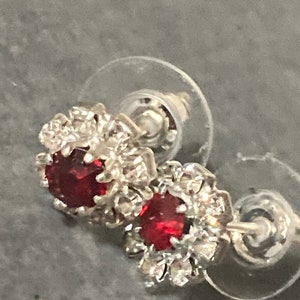 Puede incluir: Un par de pendientes de plata con una piedra roja rodeada de piedras blancas m&aacute;s peque&ntilde;as.