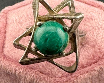 May include: A silver ring with a green gemstone set in a star-shaped design.