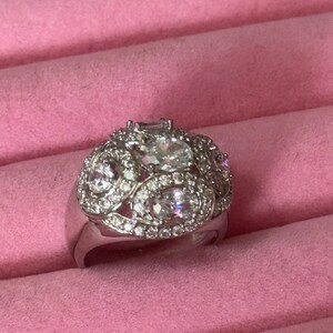 May include: A silver ring with a cluster of clear cubic zirconia stones set in a decorative design.