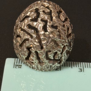 May include: A silver ring with a textured, organic design. The ring is about 2.5 cm in diameter.