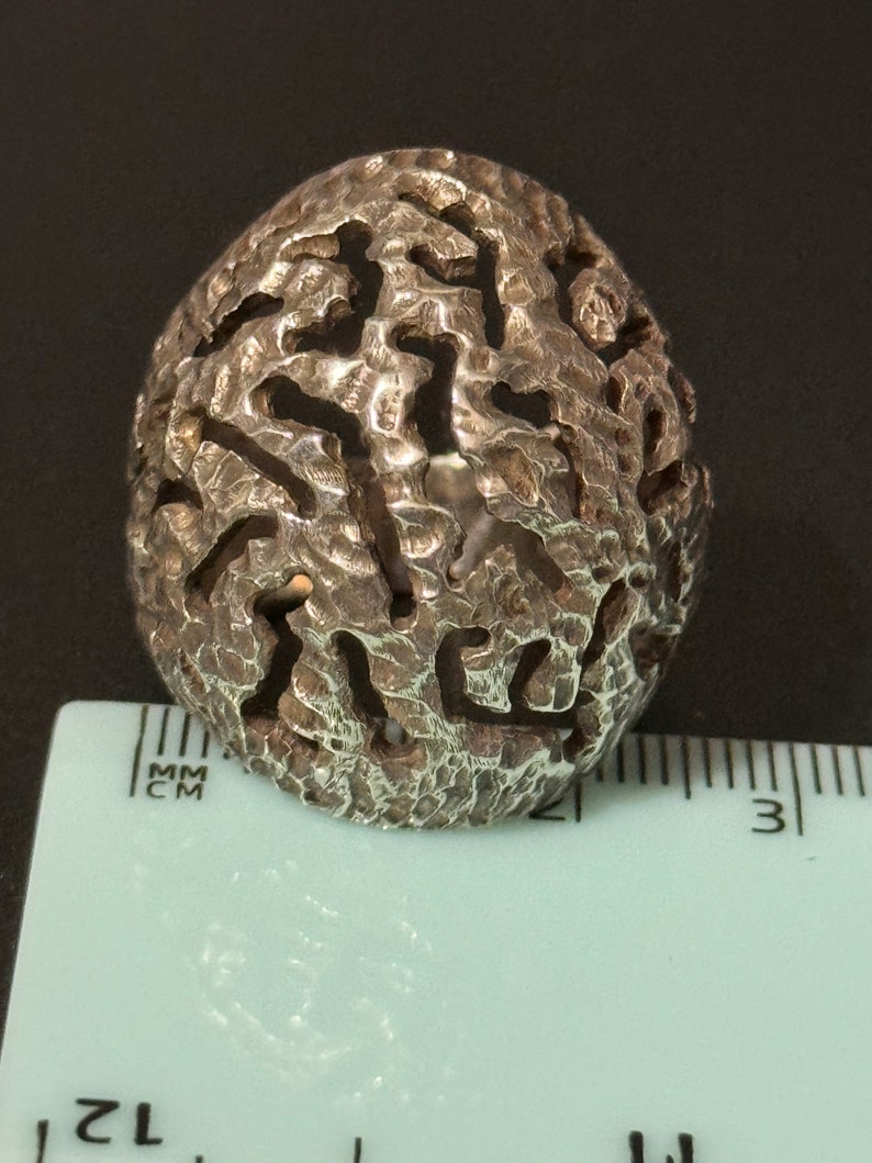 May include: A silver ring with a textured, organic design. The ring is about 2.5 cm in diameter.