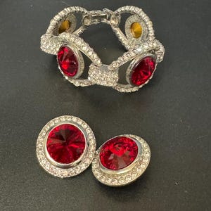 May include: A silver bracelet with three large red stones and a smaller yellow stone. Matching earrings with red stones and silver settings.