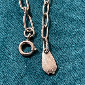 May include: A silver chain necklace with a silver pendant in the shape of a teardrop. The chain has a lobster clasp.