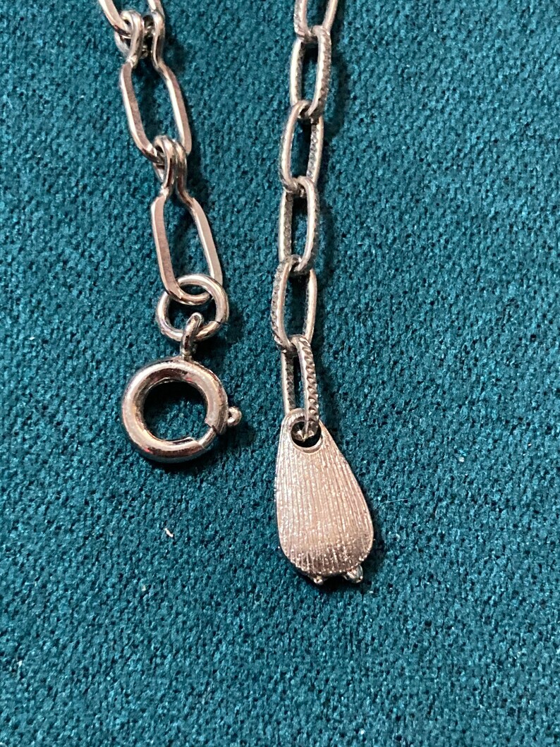 May include: A silver chain necklace with a silver pendant in the shape of a teardrop. The chain has a lobster clasp.