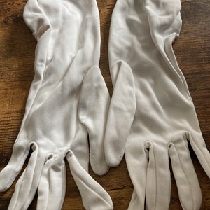 May include: A pair of white gloves, possibly made from a soft, smooth material. The gloves are displayed flat, showing the full length of the hand and fingers. The gloves look new and unused, with no visible signs of wear or damage.