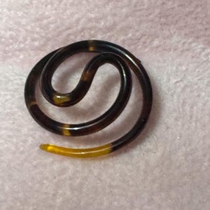 May include: A brown and yellow plastic hair clip in the shape of a coiled snake.
