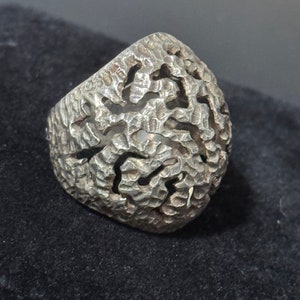 May include: A silver ring with a textured, intricate design. The ring is made of a single piece of metal and has a unique, organic shape.