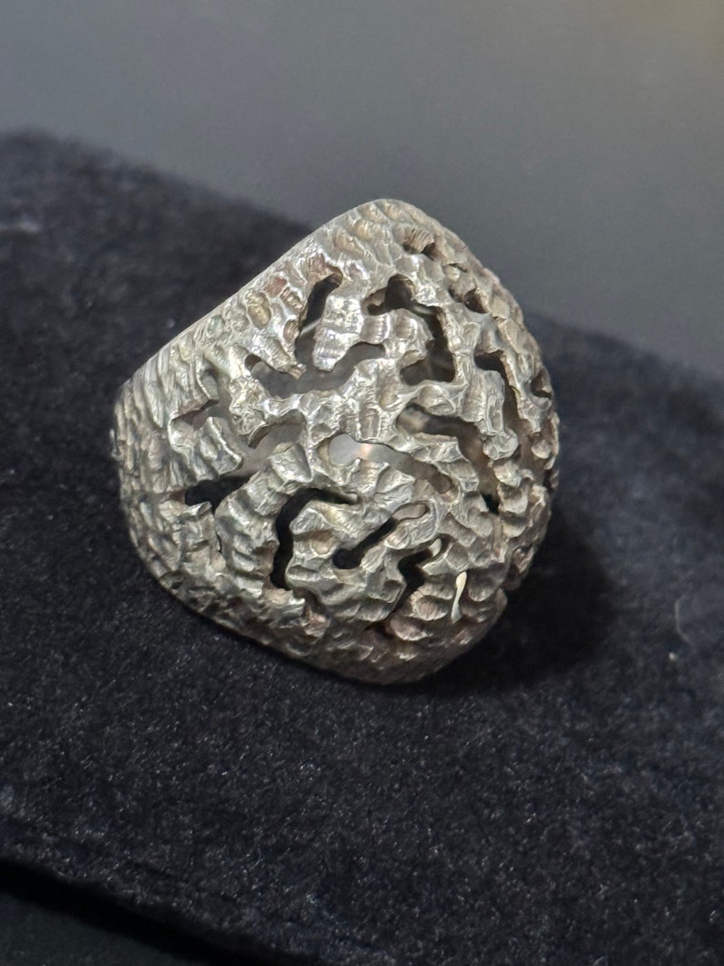 May include: A silver ring with a textured, intricate design. The ring is made of a single piece of metal and has a unique, organic shape.