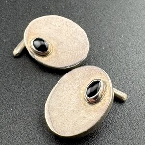 May include: A pair of silver cufflinks with black oval-shaped stones set in the centre of each cufflink.