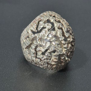 May include: A silver ring with a textured, abstract design. The ring is wide and has a unique, organic shape.