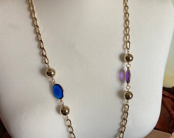 May include: A gold chain necklace with round gold beads and oval-shaped glass beads in blue, green, and purple.