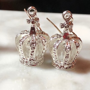 May include: A pair of silver crown-shaped earrings with a delicate design. The earrings are made of metal and have a shiny finish.
