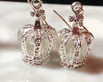 May include: A pair of silver crown-shaped earrings with a delicate design. The earrings are made of metal and have a shiny finish.