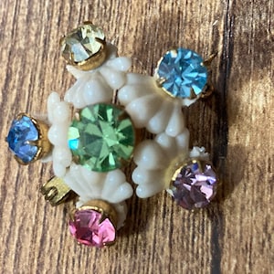 May include: A white beaded brooch with a green, blue and pink rhinestone design.