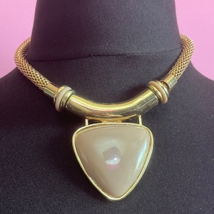 May include: A gold chain choker necklace with a large, triangular, light brown pendant.
