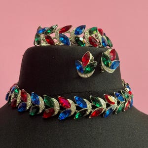 May include: A vintage jewellery set comprising a necklace, bracelet and earrings. The pieces are made of silver-tone metal and feature large, faceted stones in shades of red, green and blue.