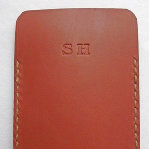 May include: A red leather phone case with a stitched edge and the initials "SH" embossed on the front.