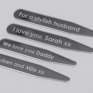 Peut inclure: Quatre attaches-cols en argent avec des messages gravés : "Pour un mari élégant", "Je t'aime, Sarah xx", "On t'aime Papa", et "Ruben et Milo xx".