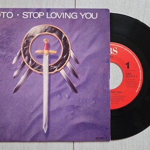 Pode incluir: Um disco de vinil de 7 polegadas e a sua capa de papel quadrada para a música Stop Loving You de Toto. A capa roxa apresenta um emblema circular central com uma espada e quatro lâminas menores. O disco tem um rótulo central vermelho.