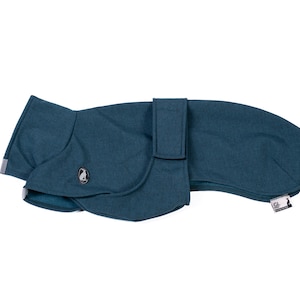 May include: A teal dog coat with a textured fabric finish, featuring a wrap-around design with a secure strap closure. The garment includes a small circular emblem with a penguin graphic and a rectangular brand tag with the text GL and a penguin.