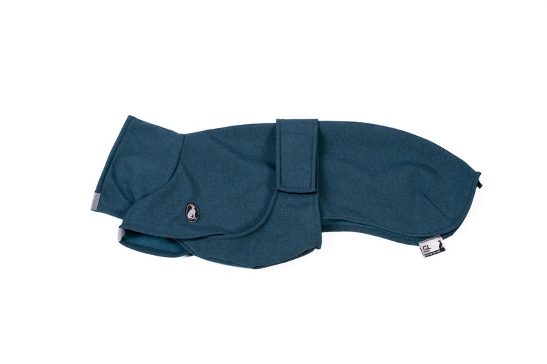 May include: A teal dog coat with a textured fabric finish, featuring a wrap-around design with a secure strap closure. The garment includes a small circular emblem with a penguin graphic and a rectangular brand tag with the text GL and a penguin.