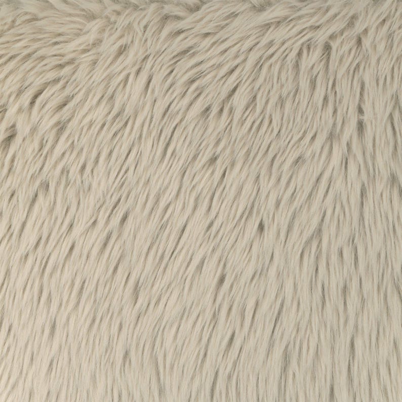 May include: Close-up of a light beige faux fur fabric. The fur has long, soft, and wavy fibers, creating a textured surface. The color is a neutral, warm tone, suitable for various home decor or craft projects.