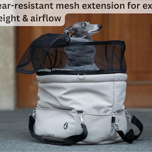 Könnte beinhalten: Eine hellgraue Haustiertasche mit einem schwarzen Netzerweiterung für zusätzliche Höhe und Luftzirkulation. Die Tasche hat einen schwarzen Schultergurt und silberfarbene Metallbeschläge. Ein kleiner Hund ist im Inneren der Tasche zu sehen.