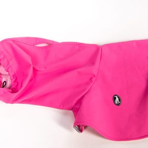 Pu&ograve; includere: Un cappotto per cani rosa acceso con collo alto dotato di coulisse regolabile, una piccola linguetta riflettente argentata e un foro per l'imbracatura. Il capo presenta una piccola toppa ovale nera con il logo di una sagoma di cane bianca.