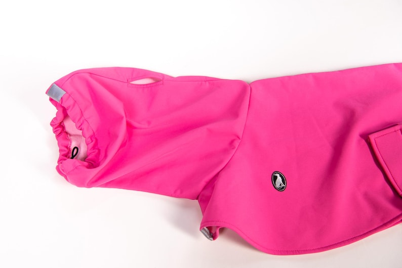 Pu&ograve; includere: Un cappotto per cani rosa acceso con collo alto dotato di coulisse regolabile, una piccola linguetta riflettente argentata e un foro per l'imbracatura. Il capo presenta una piccola toppa ovale nera con il logo di una sagoma di cane bianca.