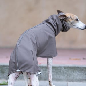 Pu&ograve; includere: Un cappotto per cani color tortora con collo alto e una cucitura riflettente lungo la schiena. Il capo presenta una piccola etichetta rettangolare del marchio vicino all'orlo posteriore ed &egrave; progettato per coprire il busto e il collo.