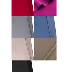 May include: A collection of seven fabric swatches in various solid colors including deep red, vibrant magenta, slate gray, dusty blue, light beige, warm taupe, and solid black. Each piece of textile displays a smooth, matte finish and folds.