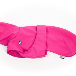 Pu&ograve; includere: Un cappotto per cani rosa acceso caratterizzato da un esterno liscio in tinta unita, una zona del colletto strutturata e una chiusura centrale a cinturino. Sul lato &egrave; visibile un piccolo logo ovale con un pinguino, insieme a una piccola etichetta.
