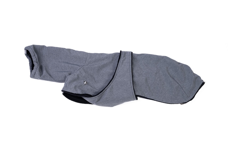 May include: A grey dog coat featuring a textured heathered fabric exterior with a solid black interior lining. The garment includes a wrap-around design with a small metallic fastener detail on the side and black trim along the edges.