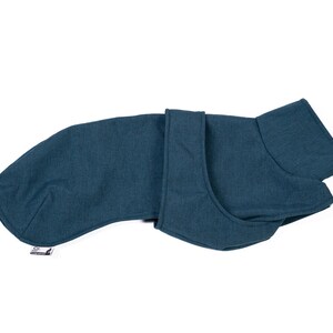 May include: A solid dark teal dog coat featuring a high collar, a wrap-around front closure, and a long back panel. The garment has a textured fabric appearance and includes a small white rectangular brand tag attached to the lower edge.