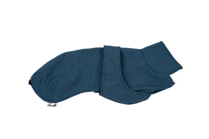 May include: A solid dark teal dog coat featuring a high collar, a wrap-around front closure, and a long back panel. The garment has a textured fabric appearance and includes a small white rectangular brand tag attached to the lower edge.