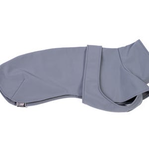 May include: A solid light gray dog coat featuring a smooth, matte finish, a high collar, and a secure wrap-around strap design. The garment includes a small rectangular brand tag with a logo on the lower left edge, providing a clean, functional look.