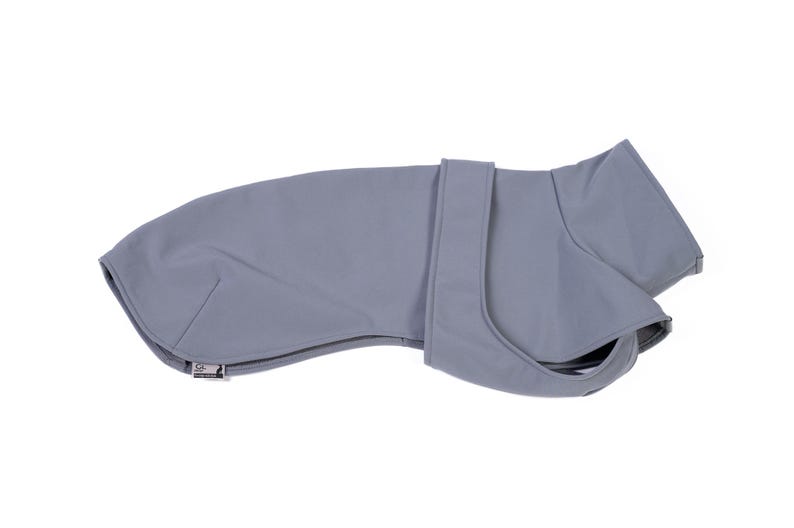 May include: A solid light gray dog coat featuring a smooth, matte finish, a high collar, and a secure wrap-around strap design. The garment includes a small rectangular brand tag with a logo on the lower left edge, providing a clean, functional look.