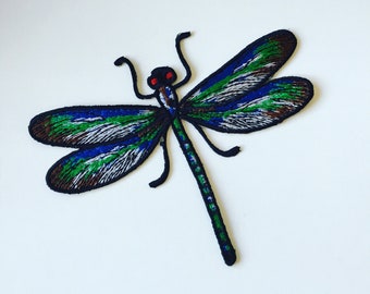 May include: A blue, green, and brown embroidered dragonfly patch with red eyes.
