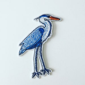Peut inclure: Patch brodé thermocollant représentant un héron bleu et blanc avec un bec orange.
