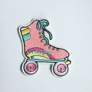 Op de afbeelding: Geborduurde patch in de vorm van een rolschaats. De roze schaats heeft turquoise, gele en gouden details. De tekst "COLOURPOP" is op de zijkant geborduurd. De wielen zijn roze met gele centra.
