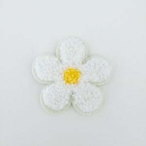 May include: A white fuzzy flower patch with a yellow center. The flower is a simple design with five petals.