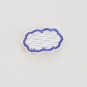 May include: A white cloud-shaped embroidered patch with a light purple border. The patch has a textured, woven appearance and is set against a plain white background. This patch is suitable for clothing or accessories.