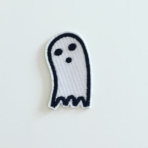 Puede incluir: Un fantasma blanco con ojos negros y una boca, bordado en un parche de tela blanca.