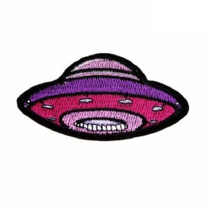 Pode incluir: Um remendo bordado de ferro de um UFO de desenho animado rosa e roxo.