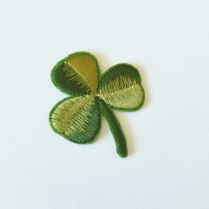 Könnte beinhalten: Ein grüner gestickter Kleeblatt-Aufnäher mit einem hellgrünen Stiel.