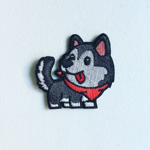 May include: Embroidered iron-on patch of a cartoon husky dog with a red bandana. The dog is black and grey with a white tongue sticking out.