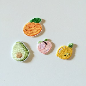 May include: Four embroidered iron-on patches featuring a peach, an avocado, a lemon, and an orange. The patches are all in a cartoon style and are perfect for adding a touch of whimsy to clothing or accessories.