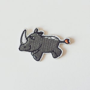 Peut inclure: Patch thermocollant brodé représentant un rhinocéros gris avec une petite queue orange.