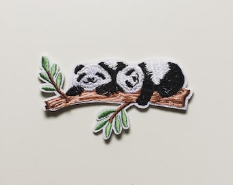 May include: Embroidered iron-on patch featuring two black and white pandas sleeping on a brown branch with green leaves.
