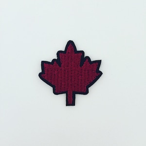 May include: A burgundy maple leaf patch with a black border. The embroidered leaf is centered on a white background. This patch is suitable for jackets, bags, or other fabric items.